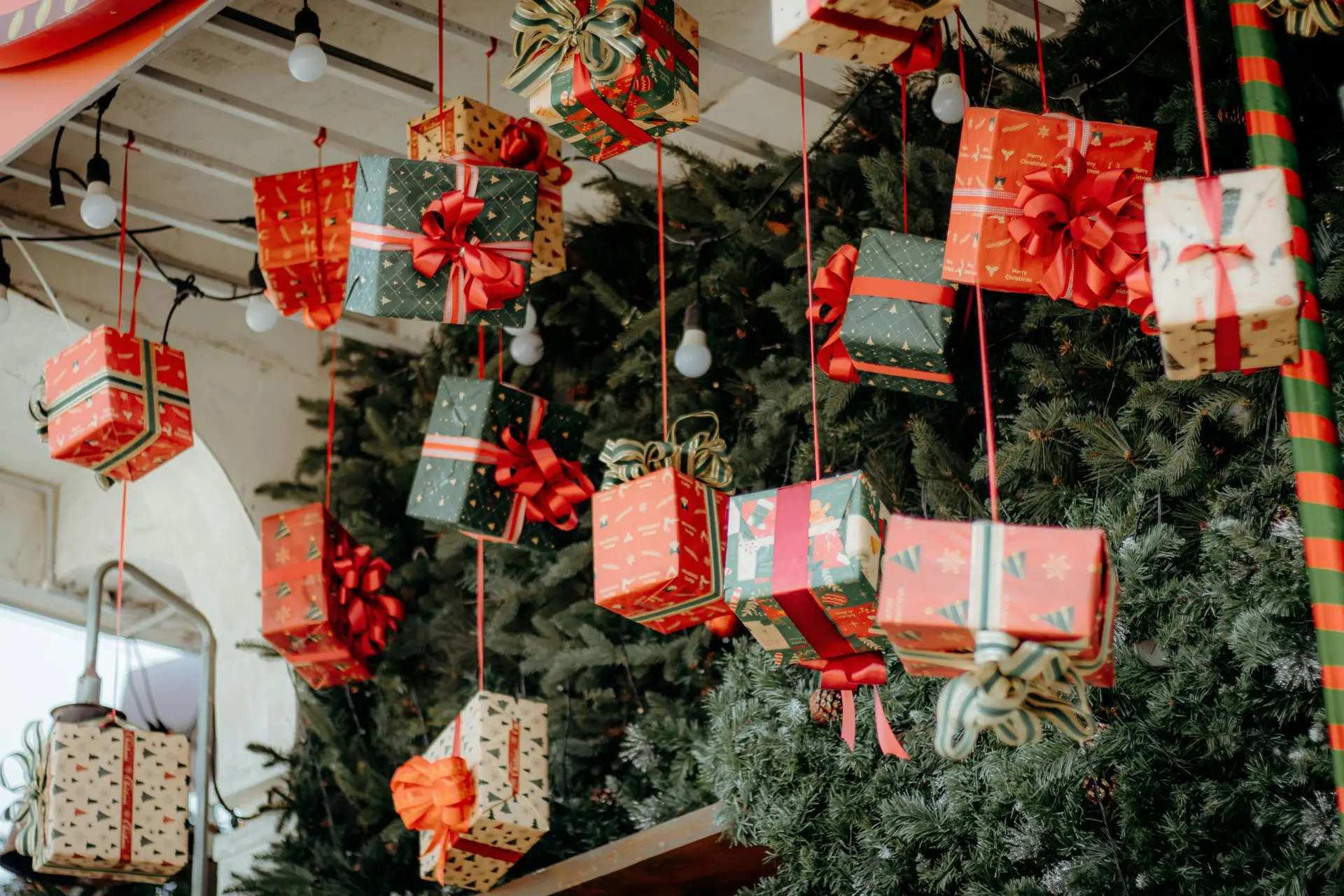 Festive Christmas gifts with ribbon bows hanging on a decorated tree.
